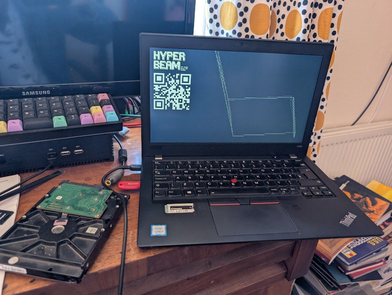 A ThinkPad laptop sits open on a desk next to an internal hard drive, displaying a HYPER BEAM text and QR code on its screen.
